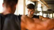 Ein junger Mann schaut sich beim Training im Fitnessstudio im Spiegel an