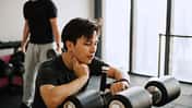 Asiatisch stämmiger Mann sitzt auf einem Fitnessgerät und checkt seinen Ruhepuls auf seiner Smartwatch Asiatisch stämmiger Mann sitzt auf einem Fitnessgerät und checkt seinen Ruhepuls auf seiner Smartwatch