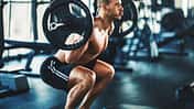 Sportlicher Mann macht oberkörperfrei eine Squatübung mit einer Langhantel im Fitnessstudio