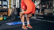 Ein junger Mann in orangener Sportkleidung dehnt sich vor dem Training im Fitnessstudio.
