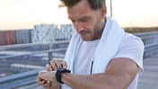 Mann mit Handtuch auf der Schulter steht draußen und schaut auf seine Smartwatch