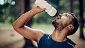 Männlicher Läufer macht im Wald eine Pause, um zu trinken