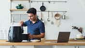 Ein Mann steht in der Küche, neben ihm ein Laptop, und bereitet Essen im Airfryer zu