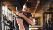 Handsome young man feeling the pain in shoulder at the gym
