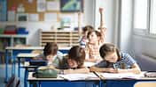 Blick in ein Klassenzimmer, Schüler sitzen an Tischen, einer meldet sich
