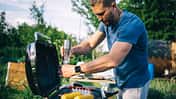 Ein Mann steht am Grill und würzt Maiskolben