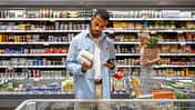 Mann steht im Supermarkt vor dem Kühlregal und schaut prüfend auf die Rückseite eines Produktes