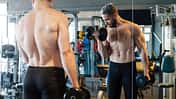 Mann steht beim Gewichtheben im Gym vorm Spiegel