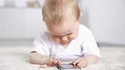 Ein Baby liegt auf dem Fußboden und spielt an einem Smartphone