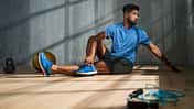 Ein Mann in blauem Sportoutfit stretcht sich vor einem grauen Hintergrund Ein Mann in blauem Sportoutfit stretcht sich vor einem grauen Hintergrund