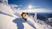 Ein Mann fährt bei blauem Himmel eine Skipiste herunter